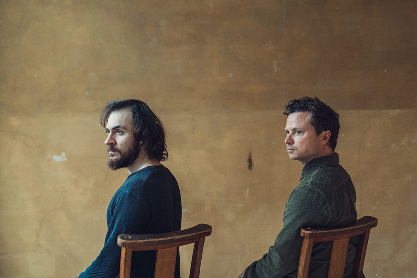 Two people that on chairs looking to the side, behind them is a brown wall. Two people that on chairs looking to the side, behind them is a brown wall.