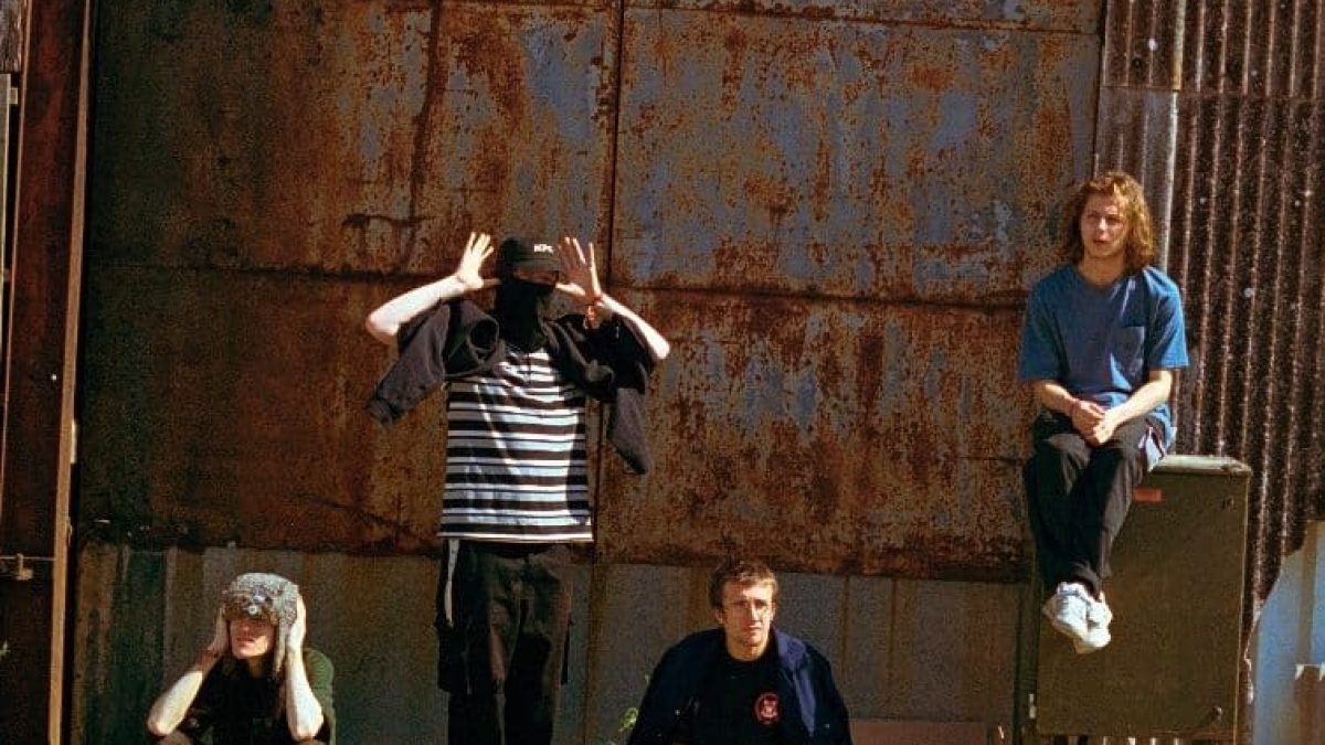 The four members of the band UNIVERSITY are stood and seated against a rusted metal background.
