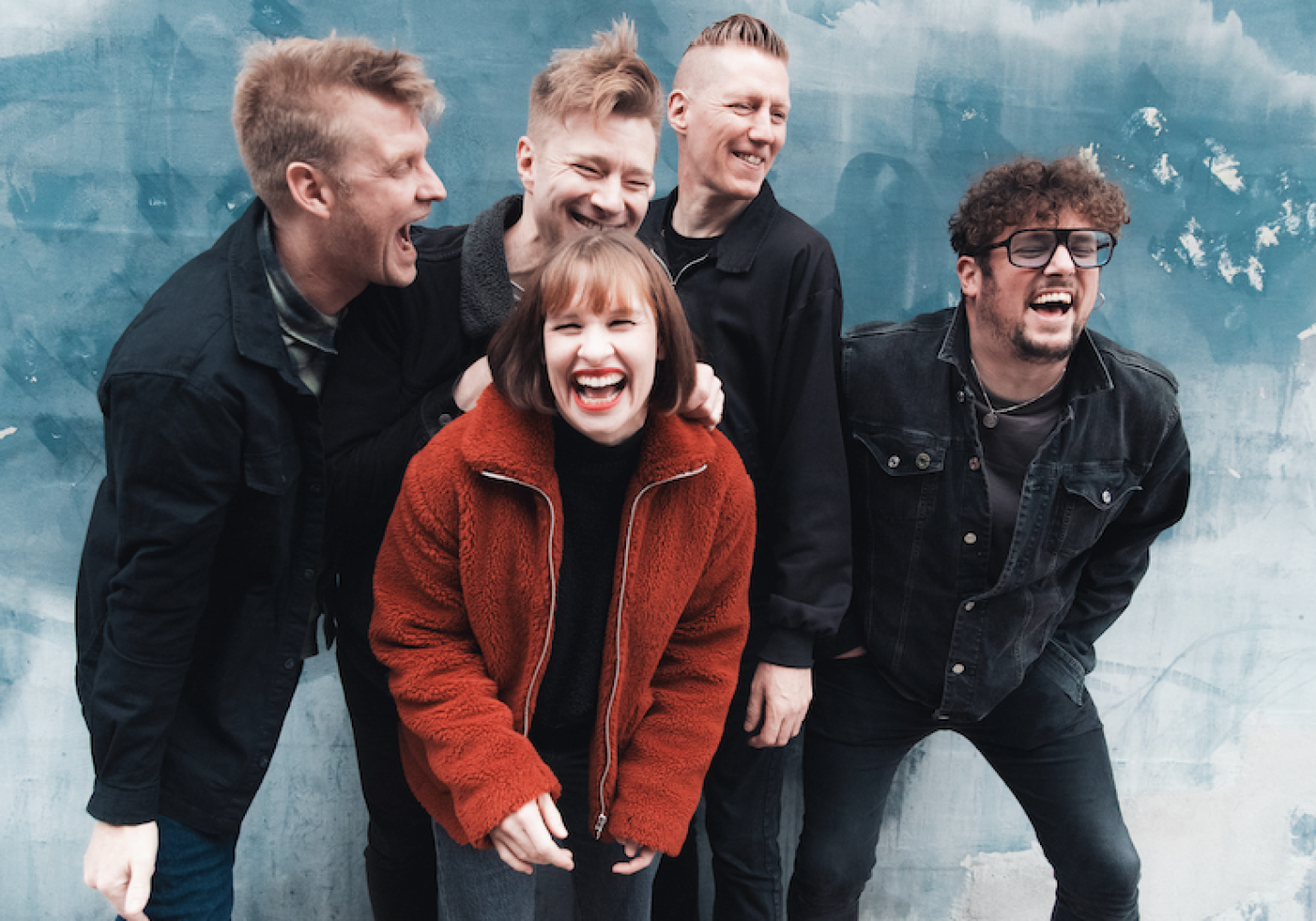 Four men and a women laughing in front of a sky blue background Four men and a women laughing in front of a sky blue background