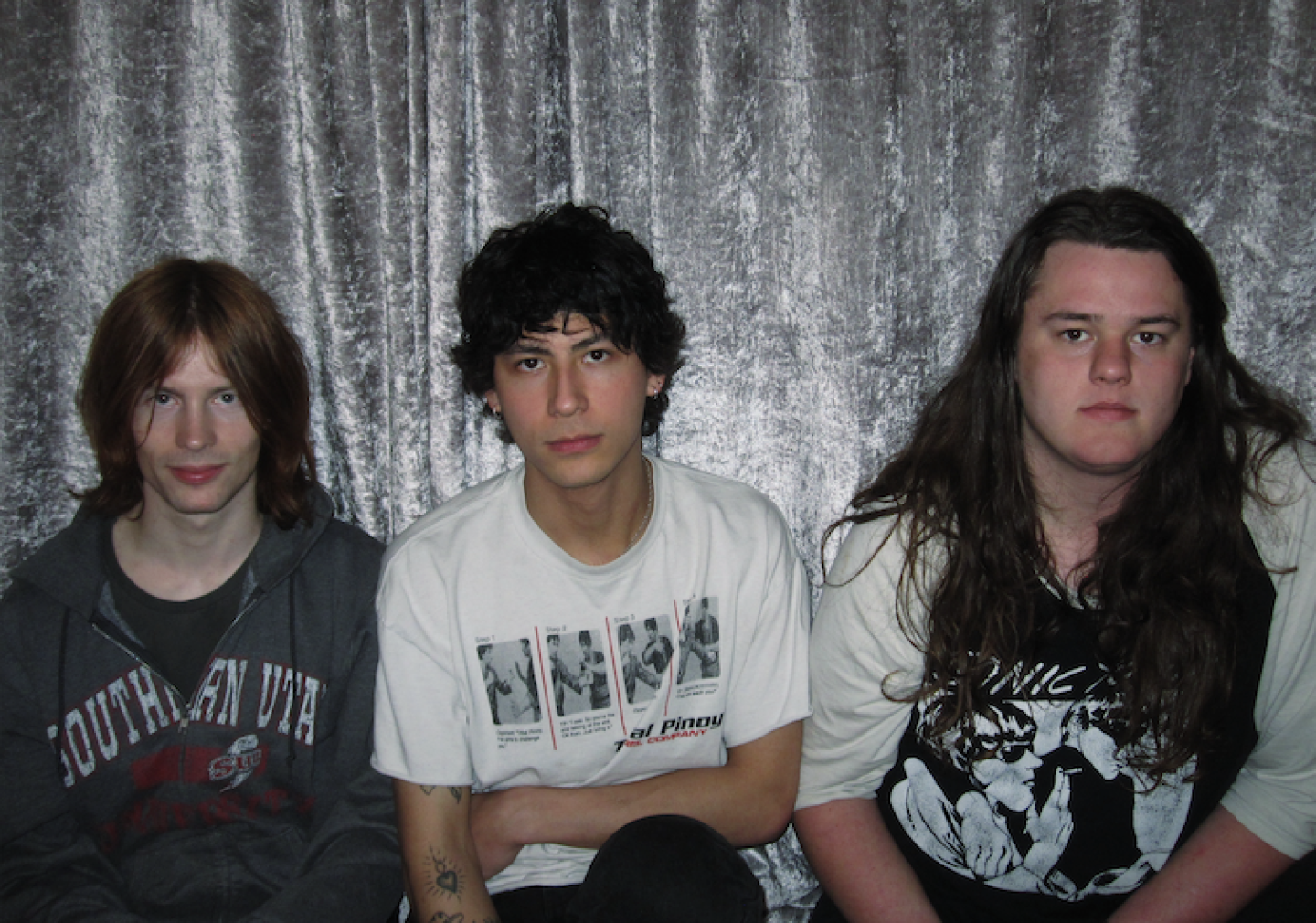 Three young people wearing t shirts sit on a sofa in front of a grey velvet curtain Three young people wearing t shirts sit on a sofa in front of a grey velvet curtain