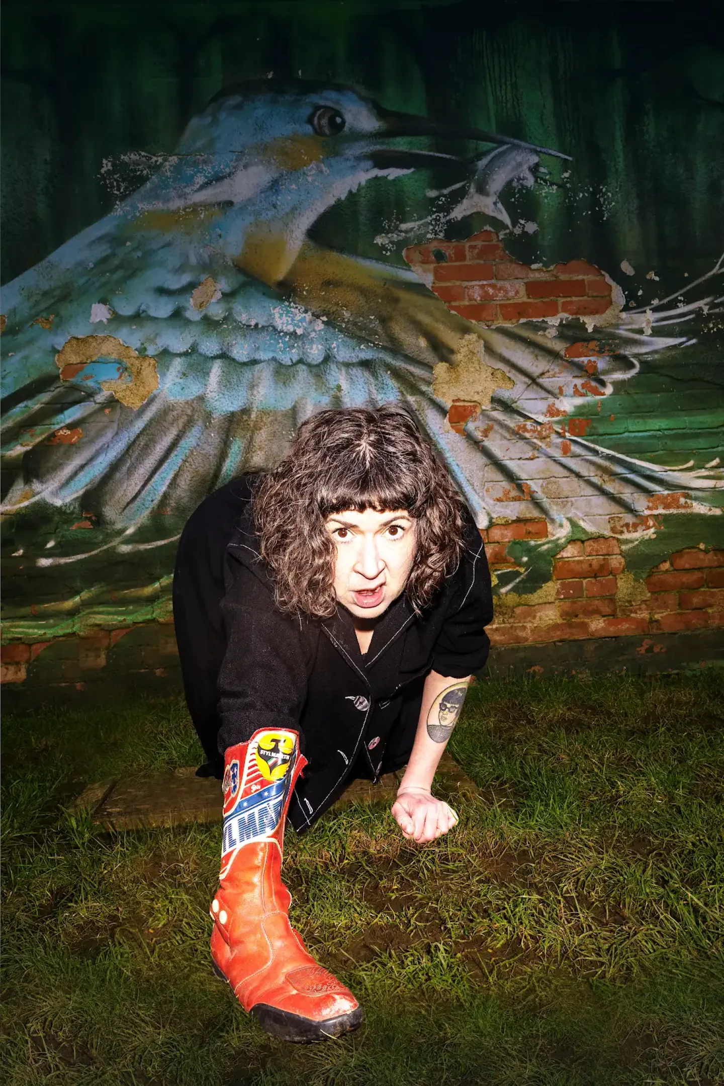 A person facing forward is crawling on grass with a red boot on their arm. A person facing forward is crawling on grass with a red boot on their arm.