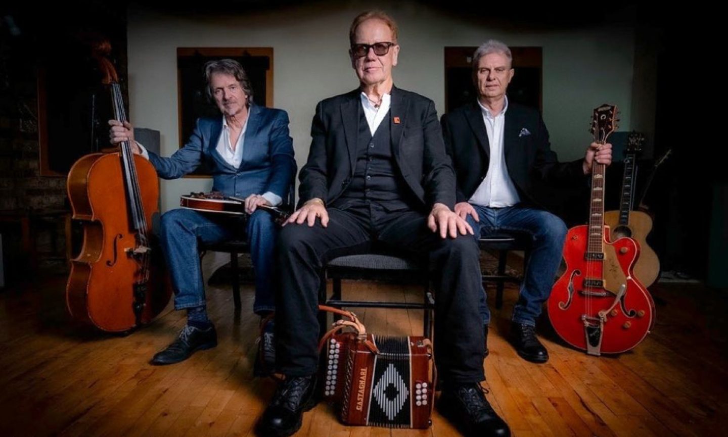 Three people sat on chairs wearing suits. Each has an instrument next to them, a double bass, and accordion, an electric guitar. Three people sat on chairs wearing suits. Each has an instrument next to them, a double bass, and accordion, an electric guitar.