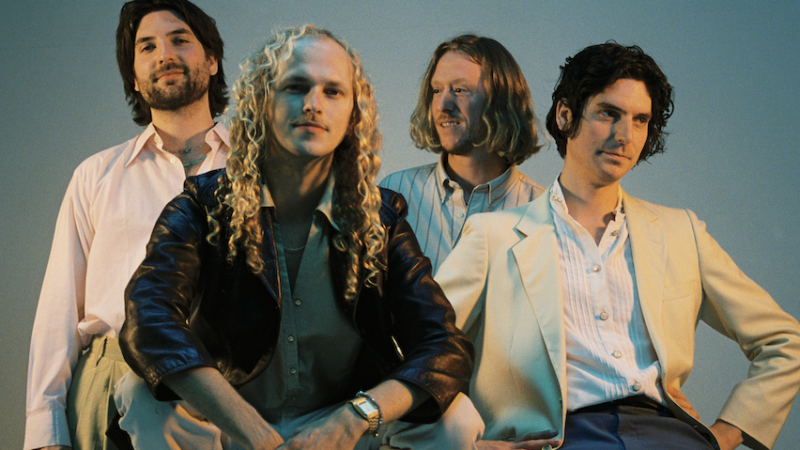 Four men stand against a grey background wearing jackets and shirts in black and cream. Four men stand against a grey background wearing jackets and shirts in black and cream.