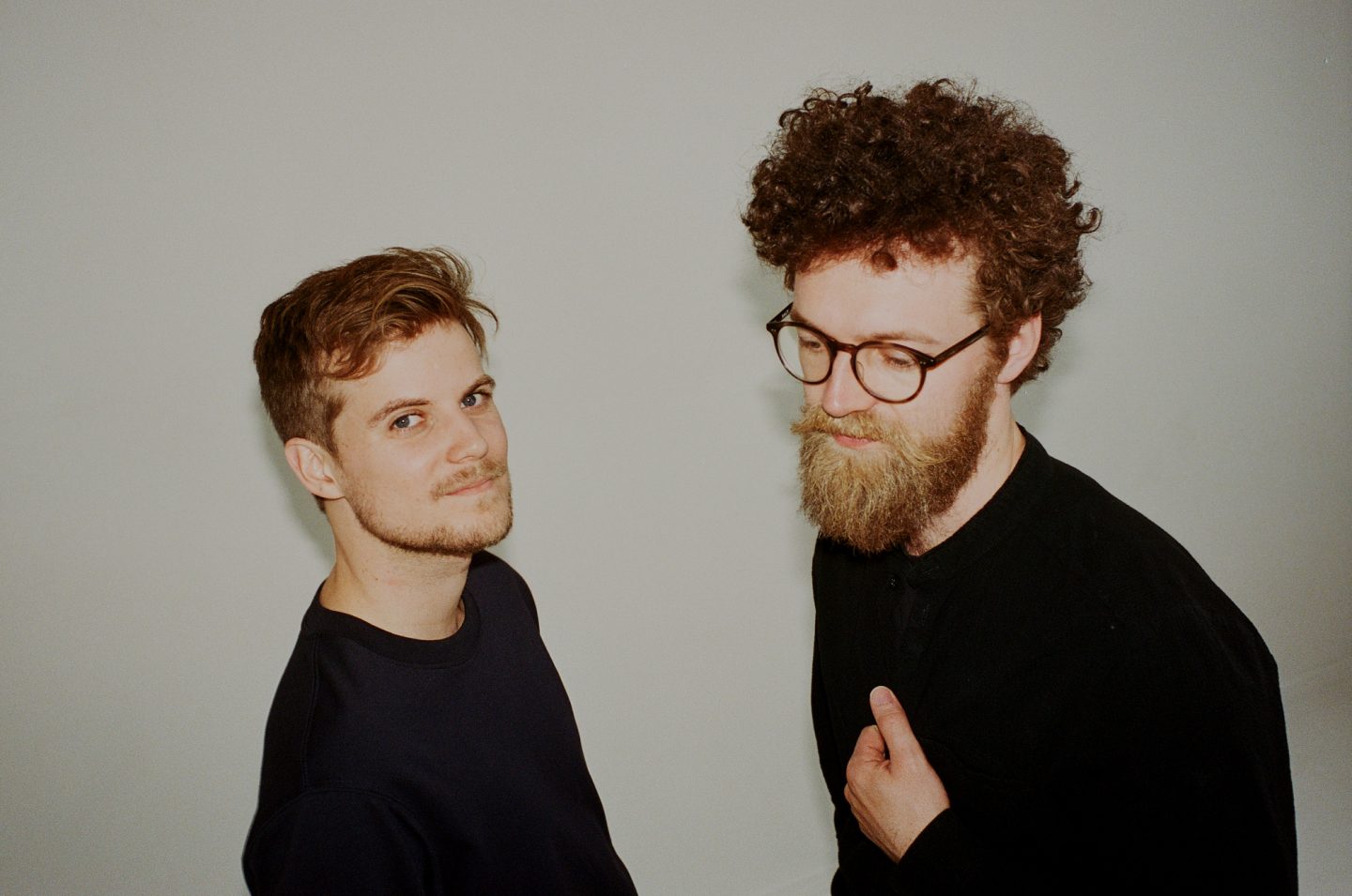 Two men wearing black t shirts stand against a grey background. Two men wearing black t shirts stand against a grey background.