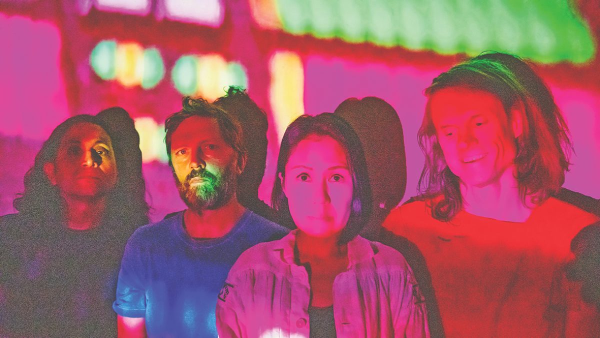 Four figures stood against a wall with a colourful light projection over them.