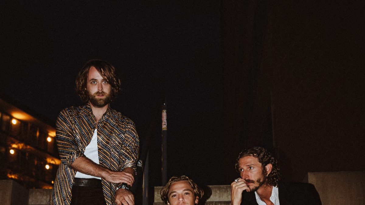 Three people sitting on outdoor steps at night, dressed in stylish, retro-inspired clothing.
