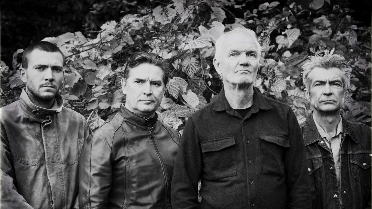 Black-and-white portrait of four men standing outdoors, facing the camera with serious expressions.