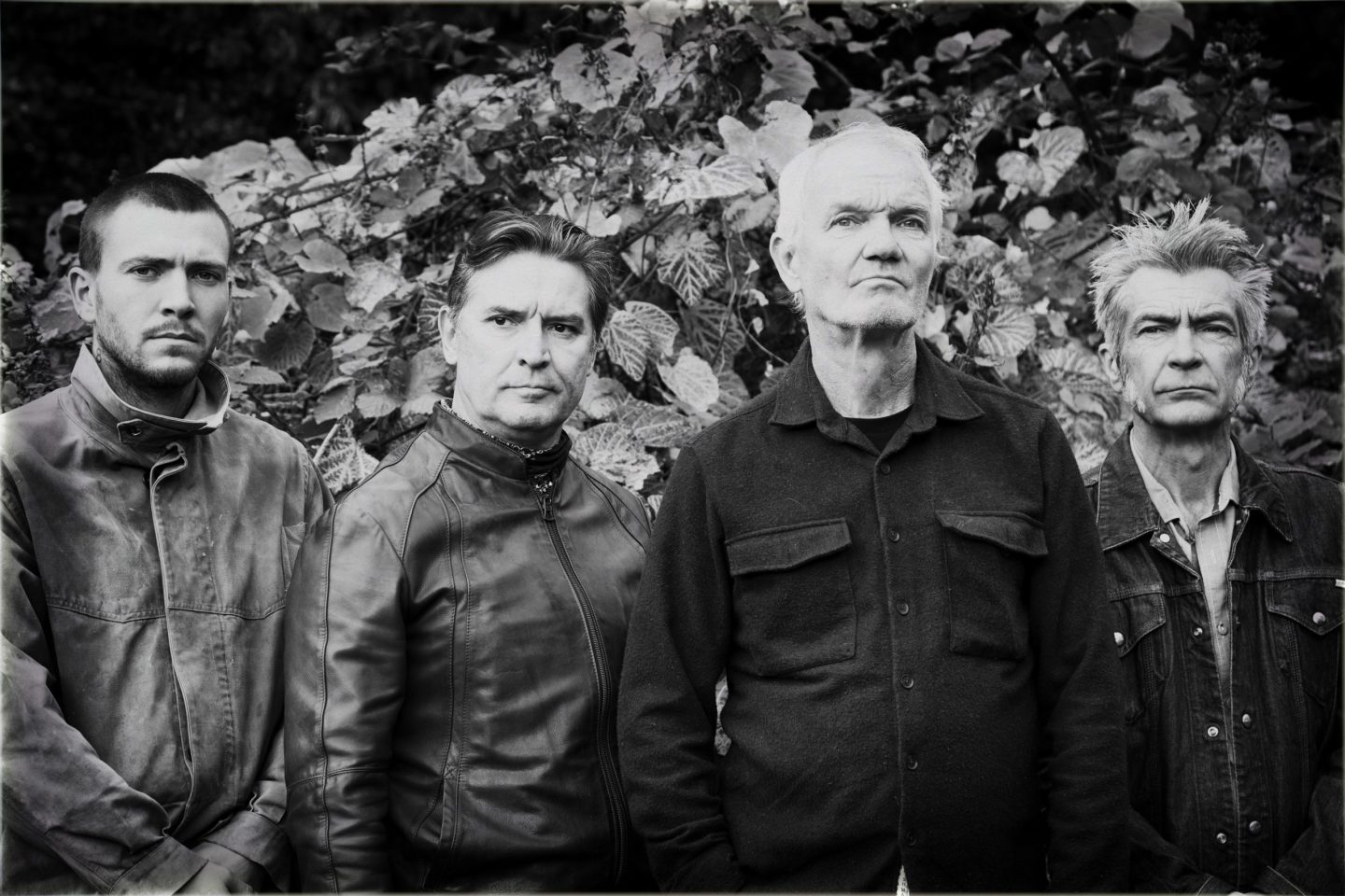 Black-and-white portrait of four men standing outdoors, facing the camera with serious expressions.