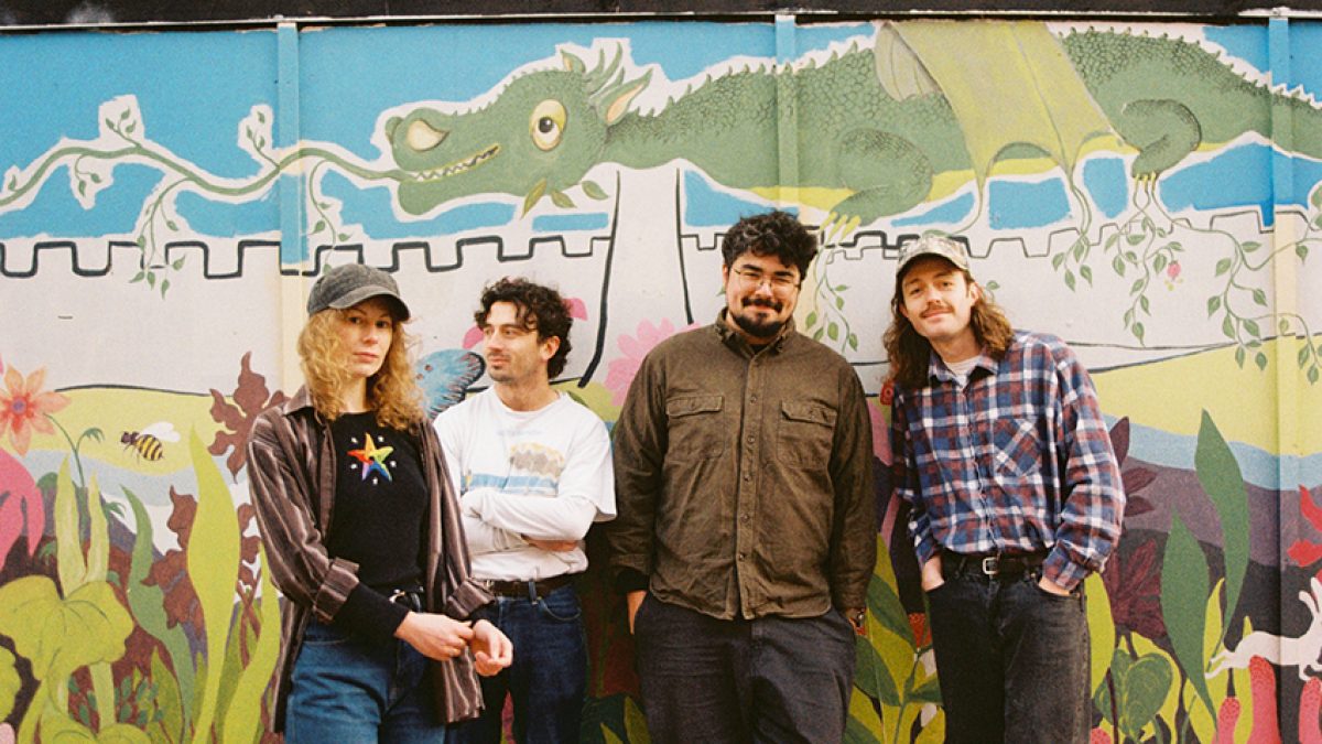 Four individuals stand in front of a colorful mural featuring a green dragon above a castle wall and plants below.