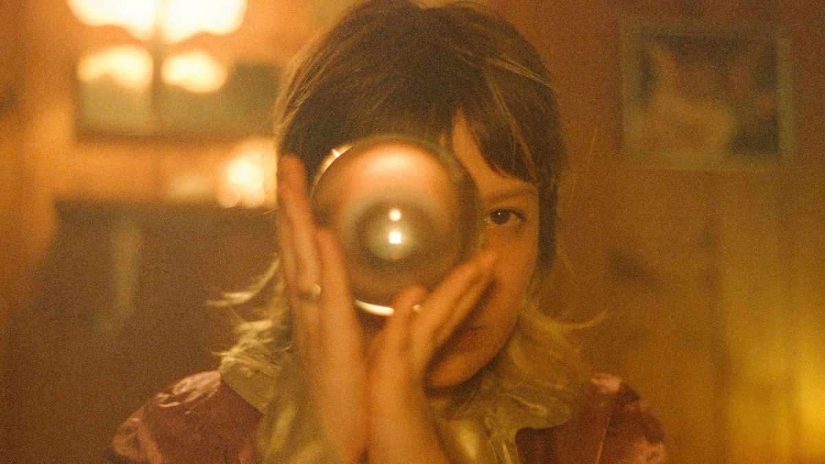 Child holding a glass orb up to one eye in warm candlelight