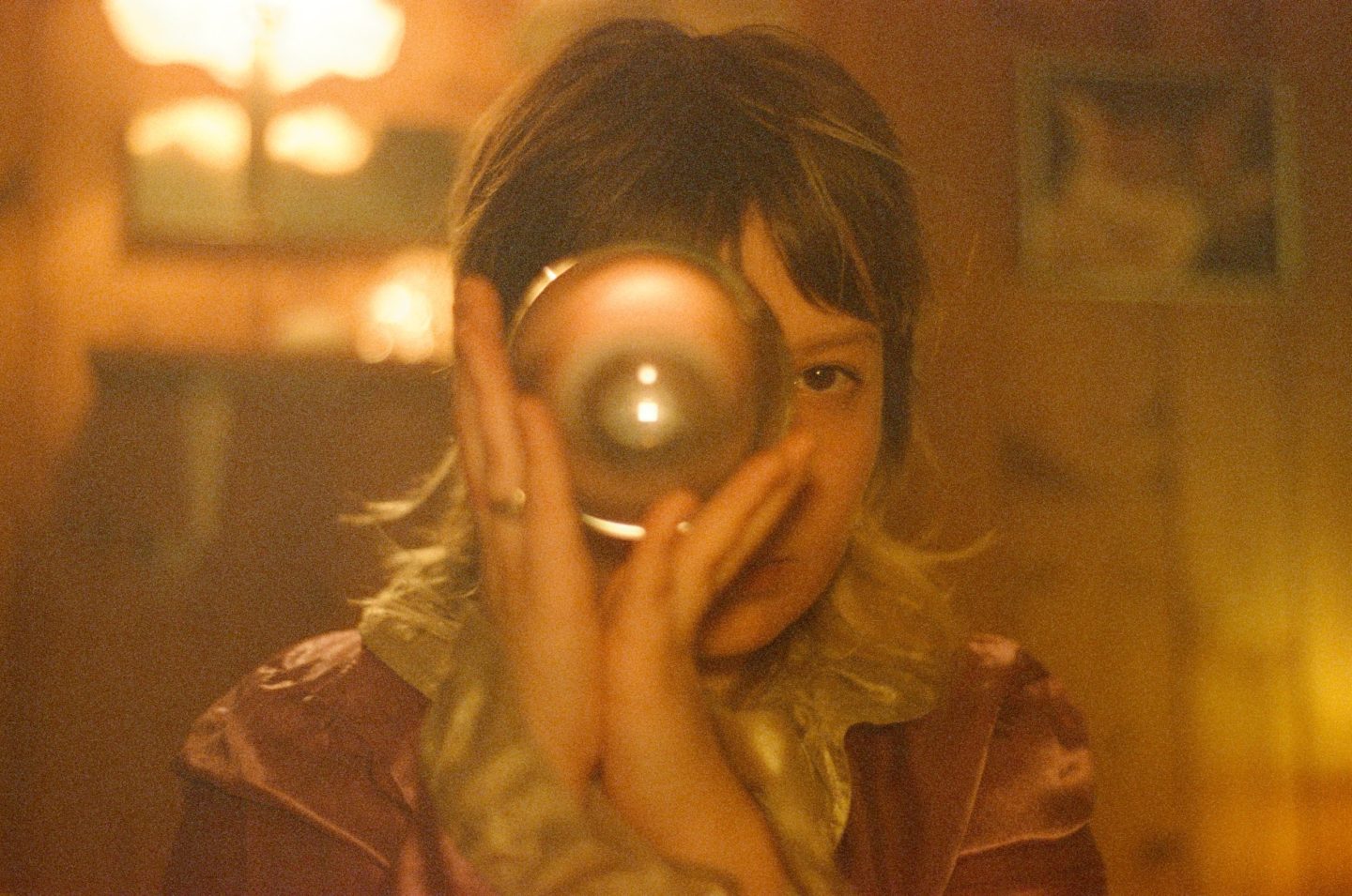Child holding a glass orb up to one eye in warm candlelight