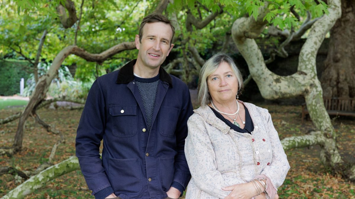 wo people standing side-by-side outdoors, likely in a park or garden