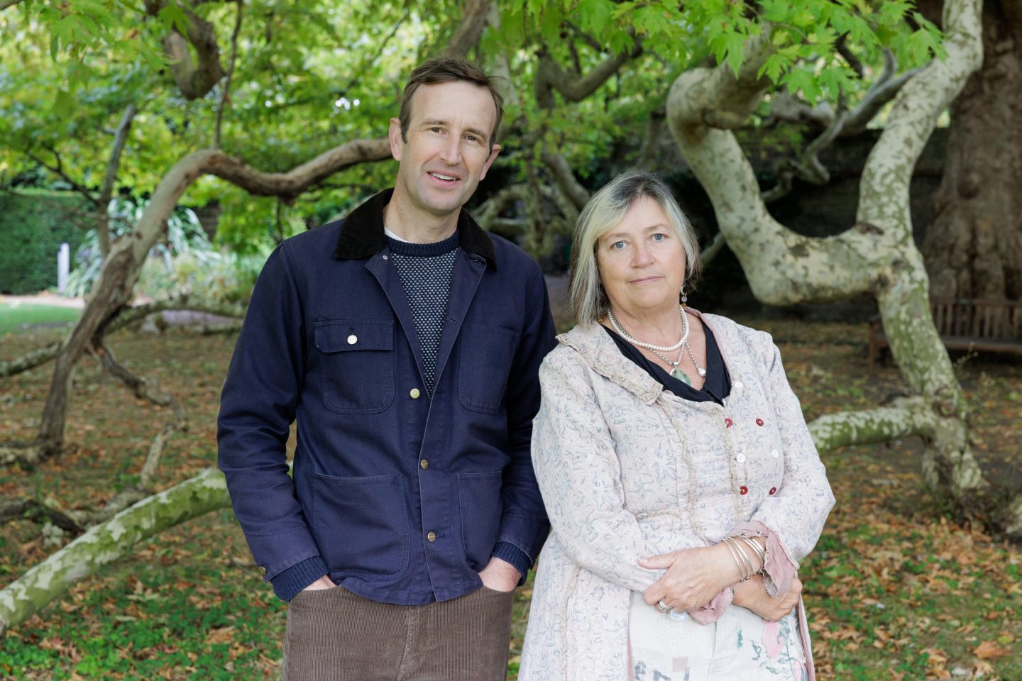wo people standing side-by-side outdoors, likely in a park or garden