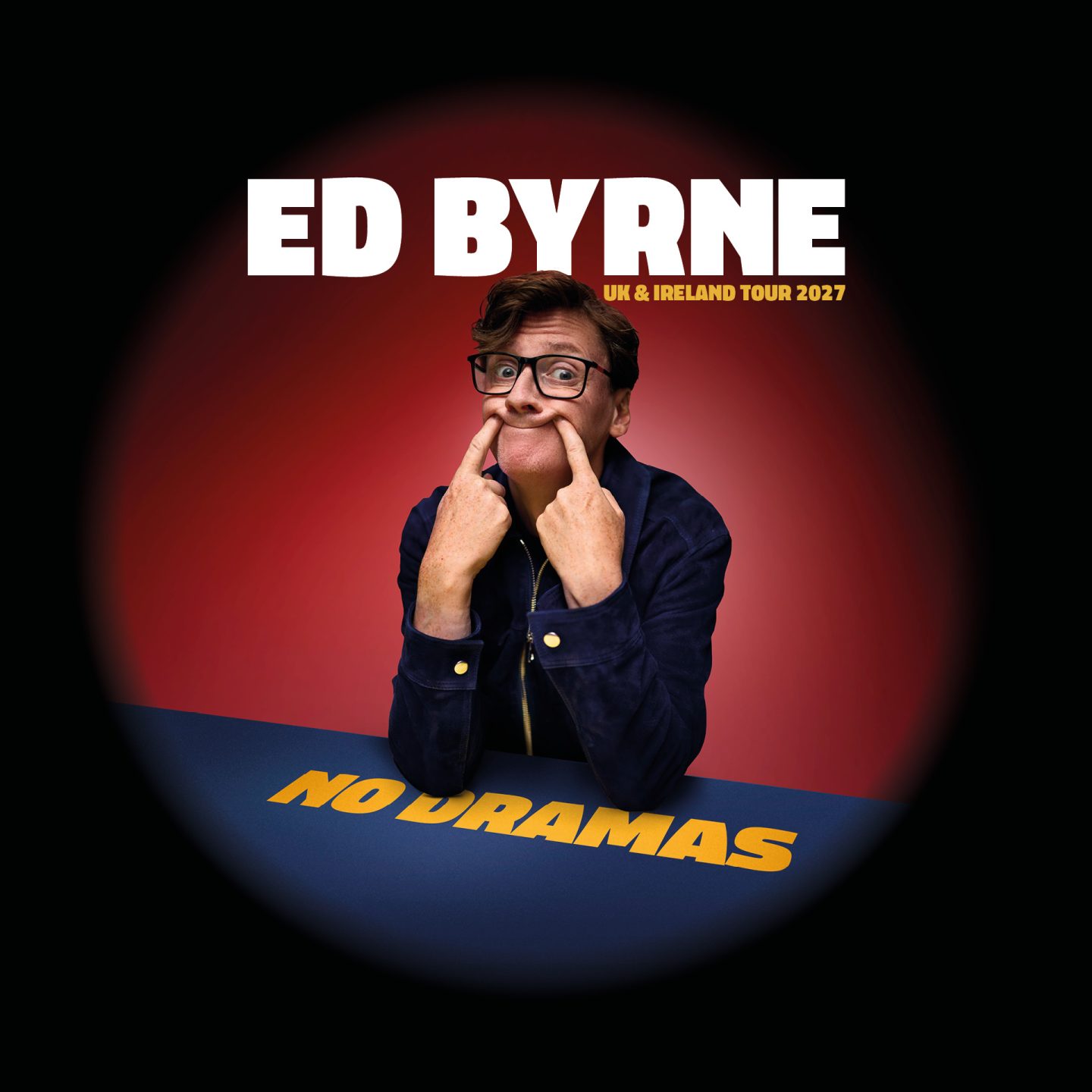 Poster for No Dramas, Ed Byrne's UK & Ireland Tour 2027. A bespectacled comedian in a navy jacket leans on a blue table labelled “NO DRAMAS,” pulling the corners of their mouth into an exaggerated smile. Large white text reads “ED BYRNE” against a red spotlight-style background that fades to black around the edges.